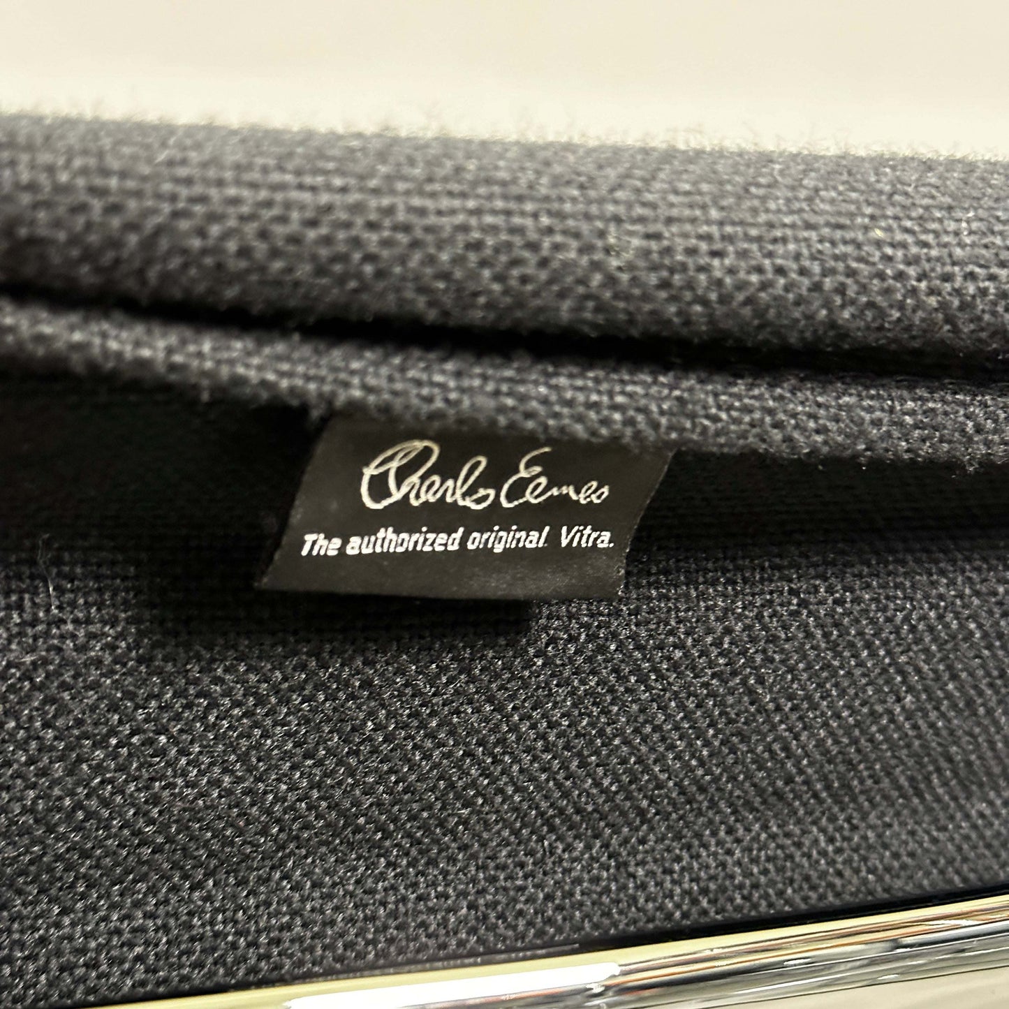 Close-up of black hopsak fabric and chrome frame on Vitra EA 108 Eames Alu Chair tag