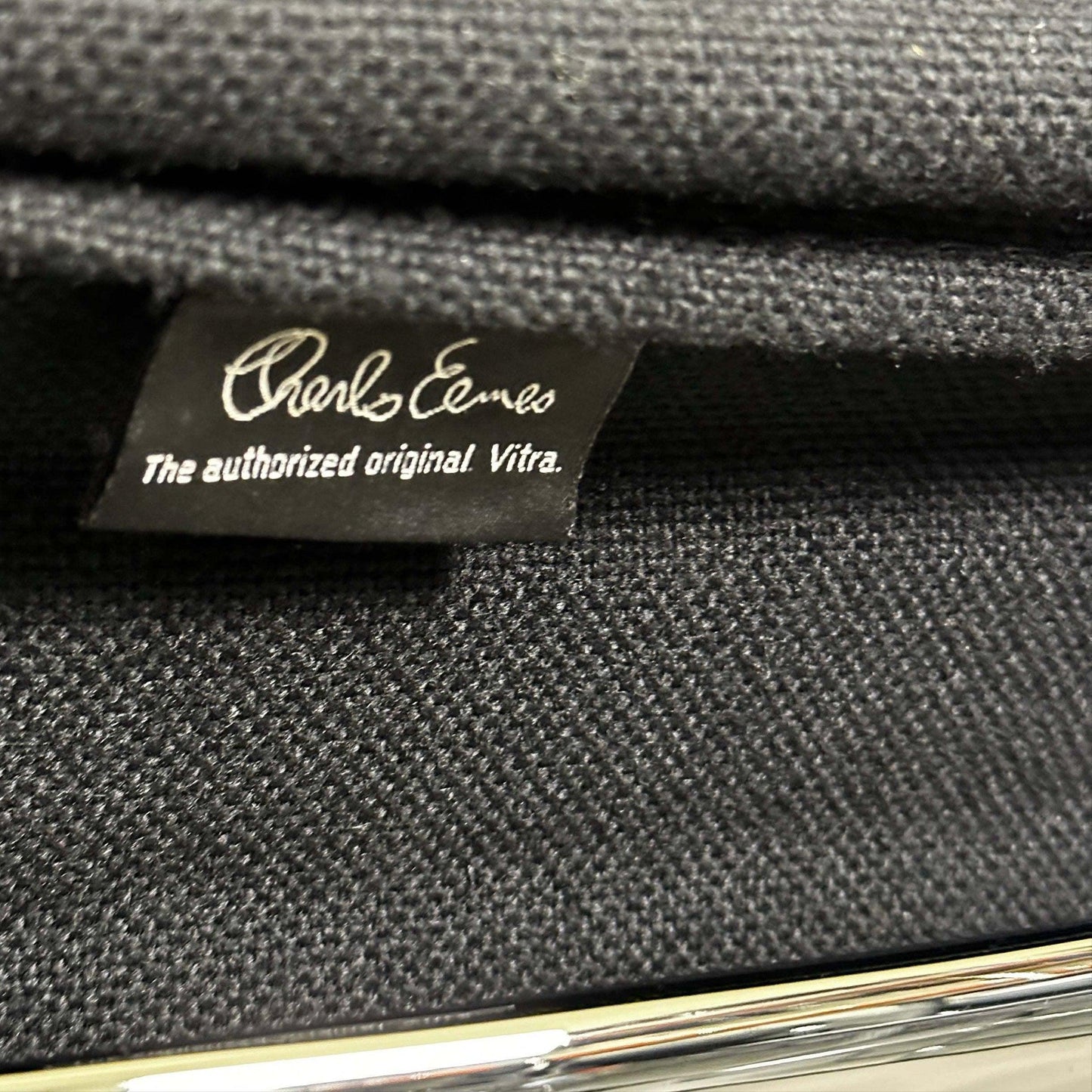 Close-up of black hopsak fabric and chrome frame on Vitra EA 108 Eames Alu Chair tag