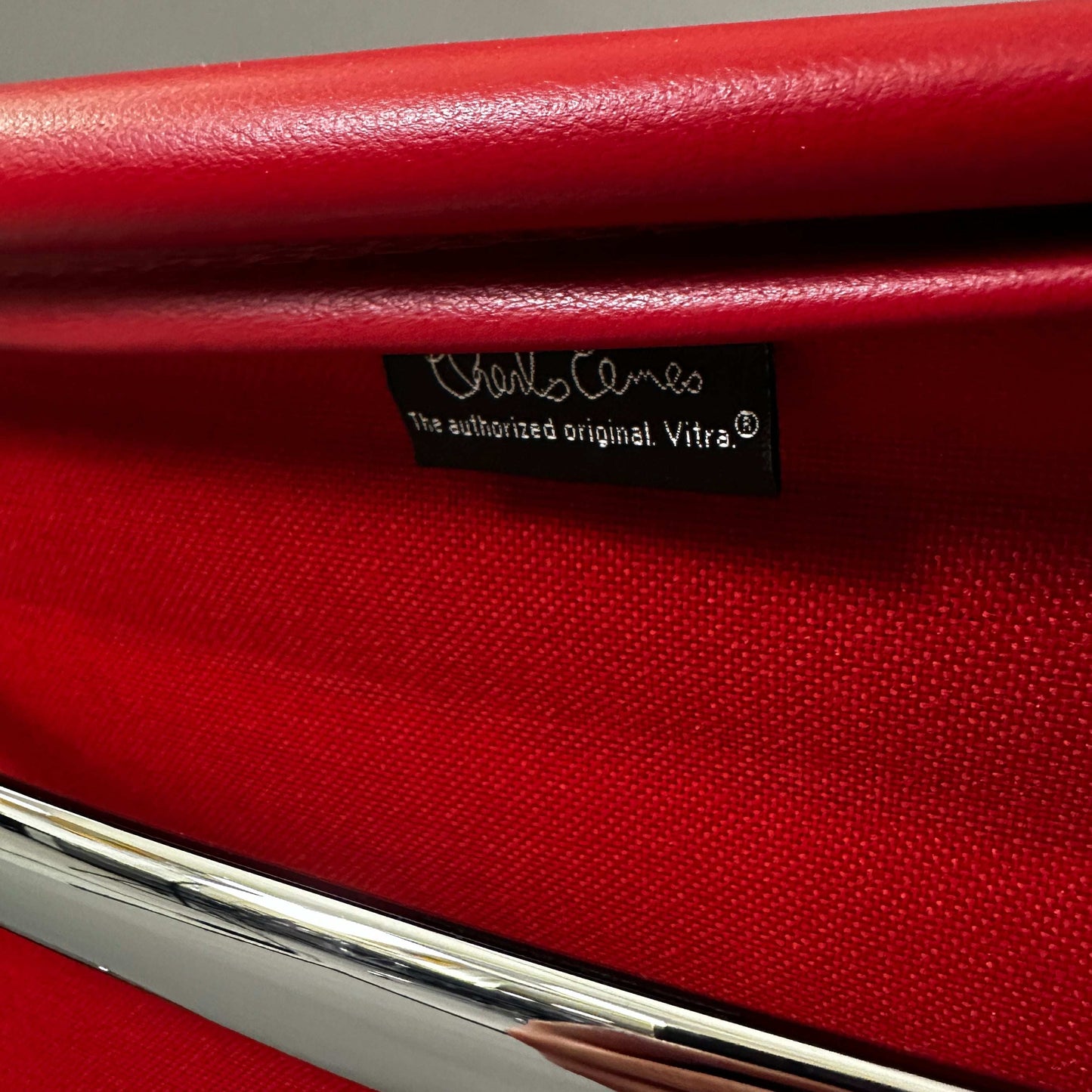 Close-up of red leather Vitra EA 108 swivel chair with chrome frame and Charles Eames label