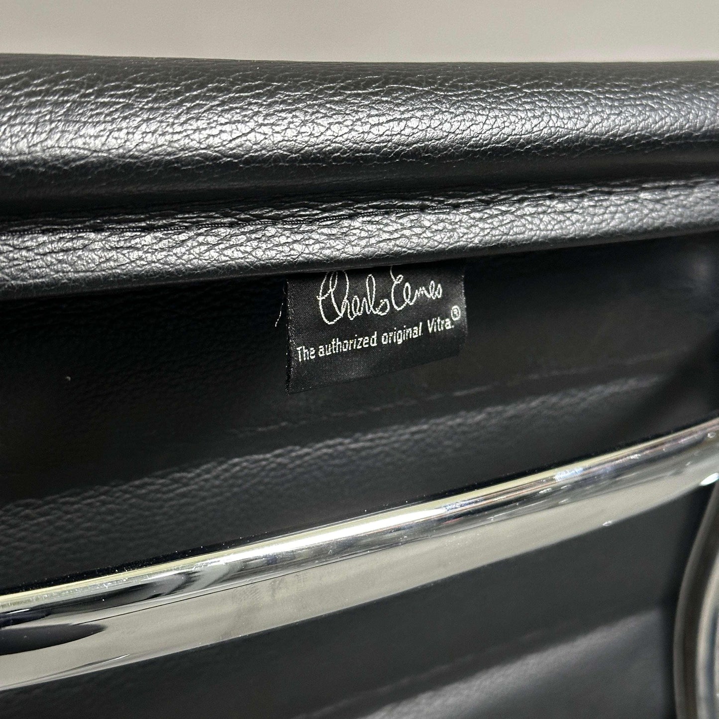Close-up of black leather seat with Charles Eames label and chrome aluminum frame of Vitra EA 108 chair