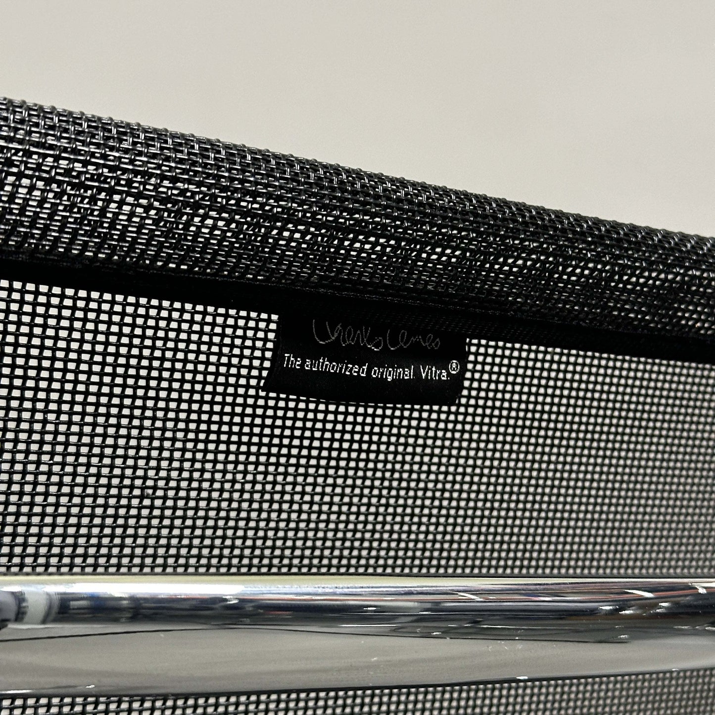 Close-up of black mesh backrest with Vitra EA 108 label and chrome frame of Charles Eames Alu Chair.