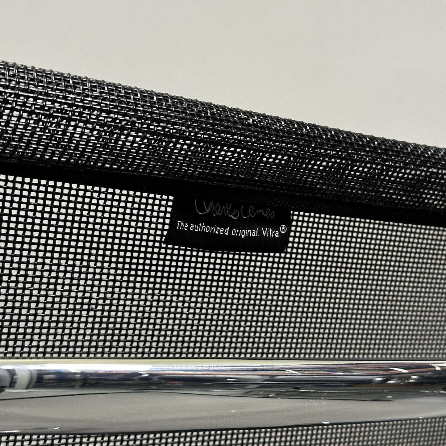 Close-up of black mesh backrest with Vitra EA 108 label and chrome frame of Charles Eames Alu Chair.