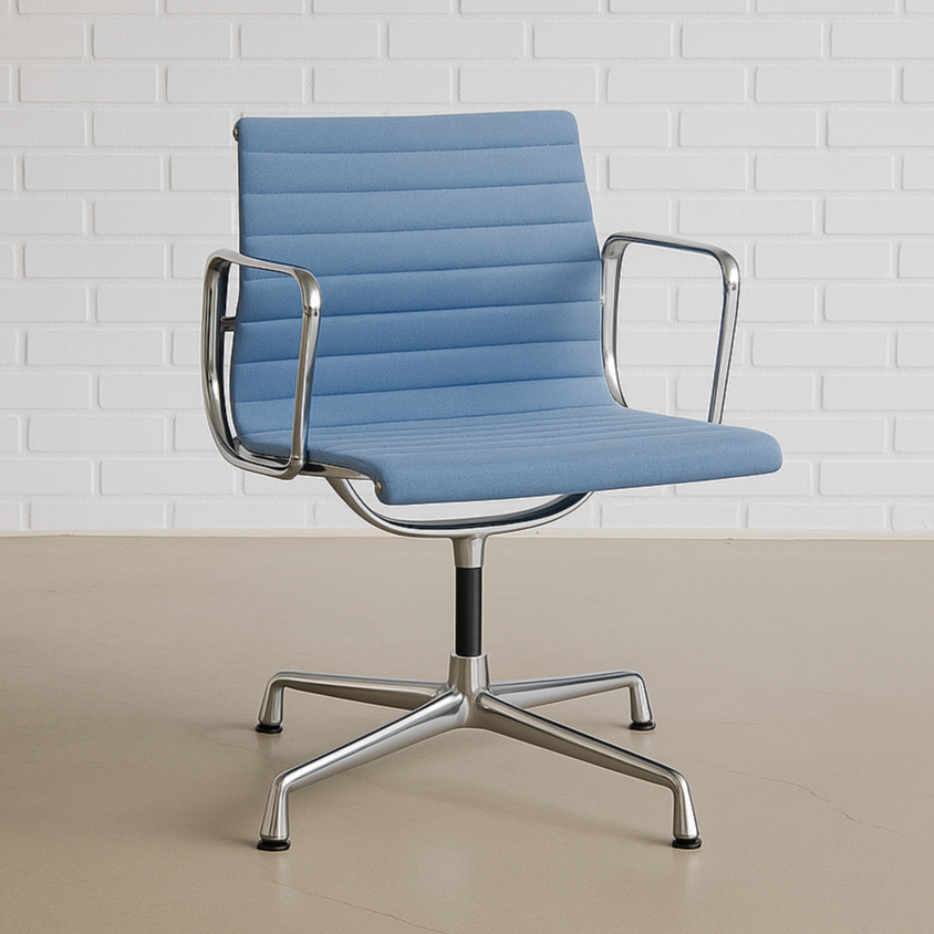 Vitra EA 108 Bürostuhl mit petrolblauem Velours-Bezug und chromfarbenem Drehgestell vor weißer Backsteinwand