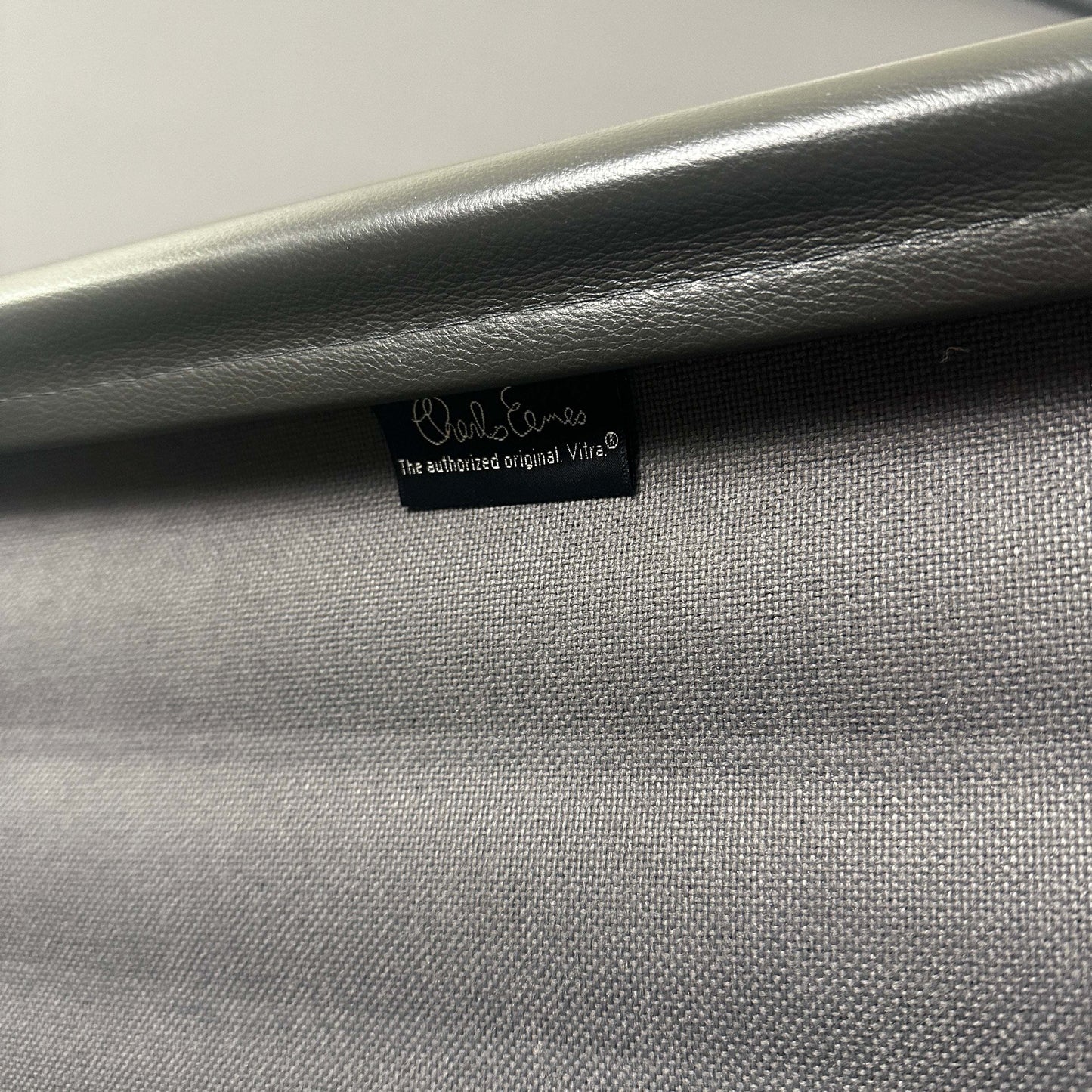 Nahaufnahme des grauen Lederbezugs und des polierten Aluminiumgestells des Vitra EA 112 Eames Alu Chair mit Vitra-Label