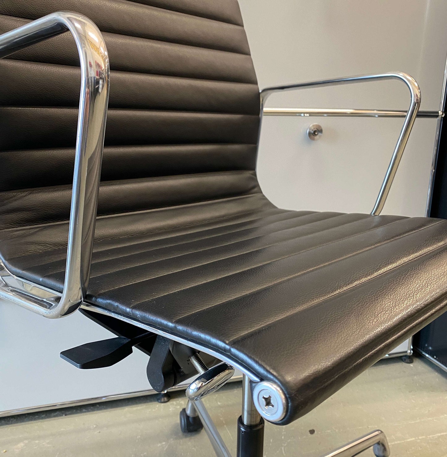 Close-up of Vitra EA 119 black leather office chair with high back and polished aluminum frame