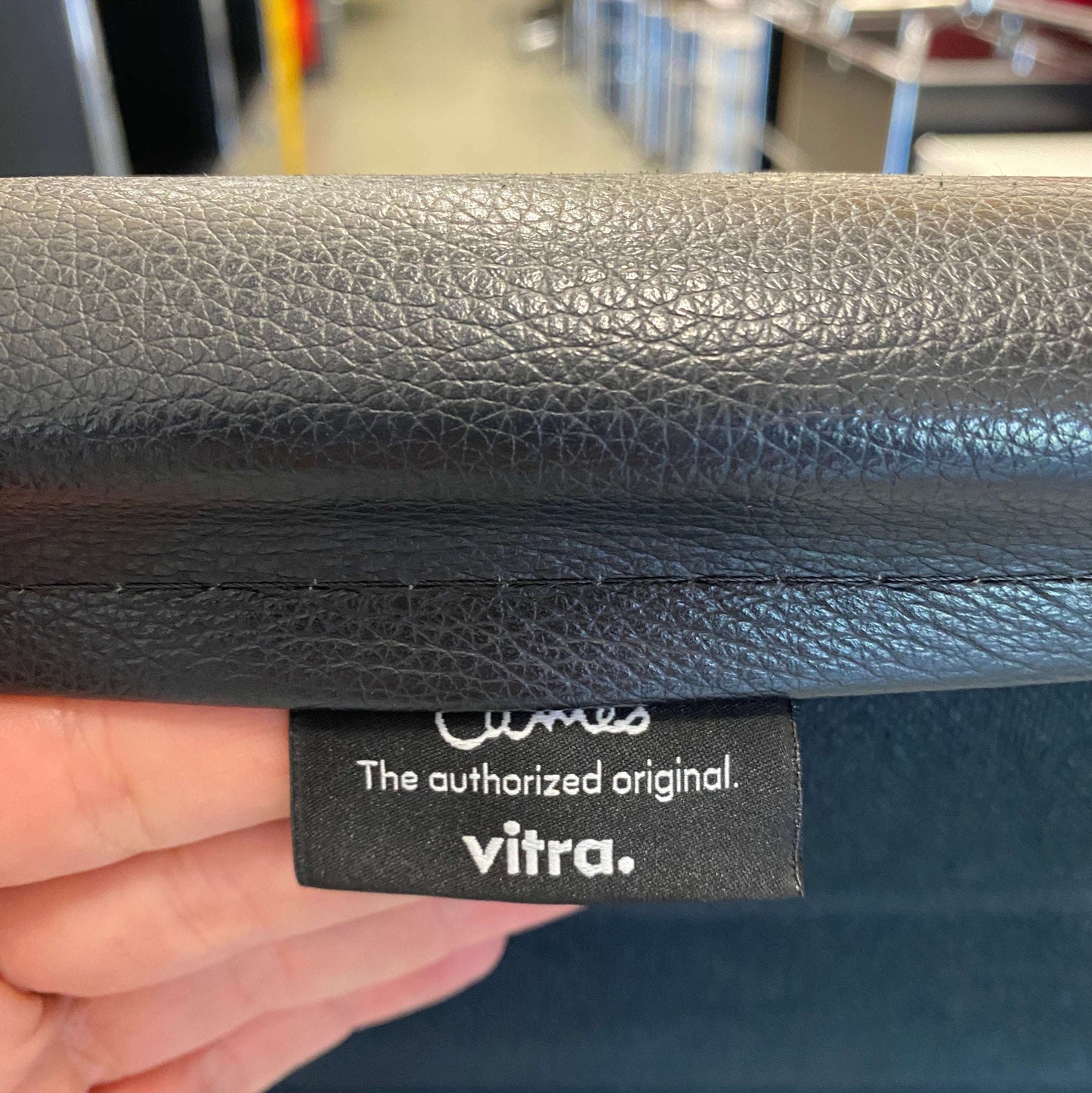 Close-up of black leather upholstery and Vitra EA 119 original label on chair with polished aluminum frame