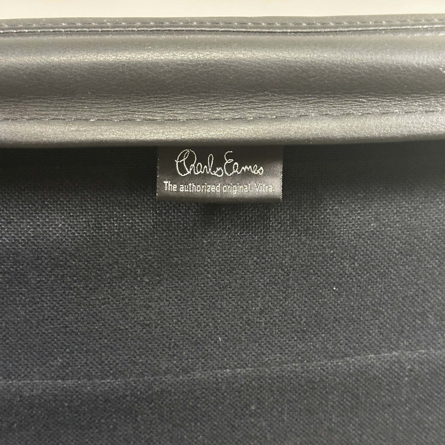 Close-up of black leather tag on Vitra EA 216 Eames Alu Chair soft pad upholstery