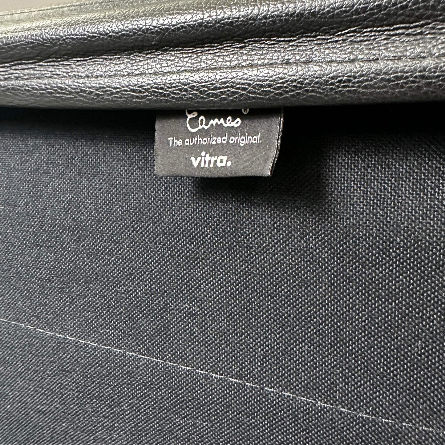 Detailaufnahme des schwarzen Lederbezugs und Vitra Eames EA 219 Labels am polierten Aluminiumstuhl