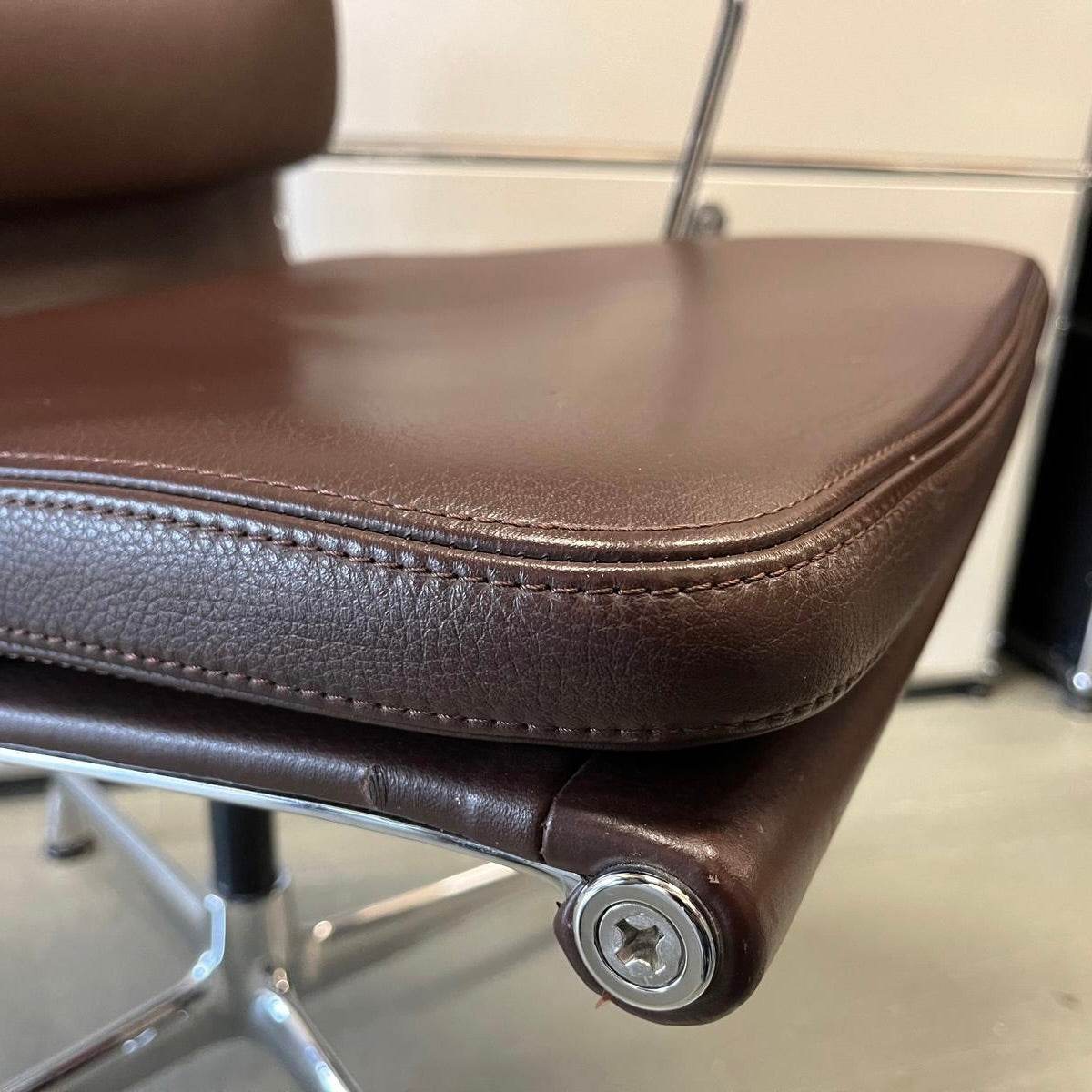 Close-up of brown Vitra EA Soft Pad Chair seat cushion with chrome swivel base