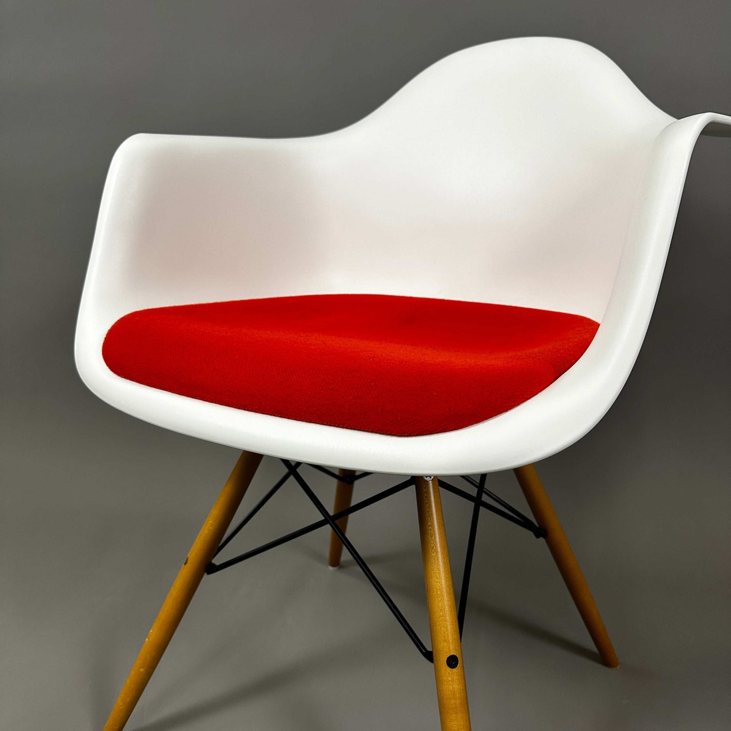 Vitra Eames Plastic Armchair mit weißer Kunststoffschale, rotem Hopsak-Sitzpolster und Holzgestell mit Metallverstrebungen