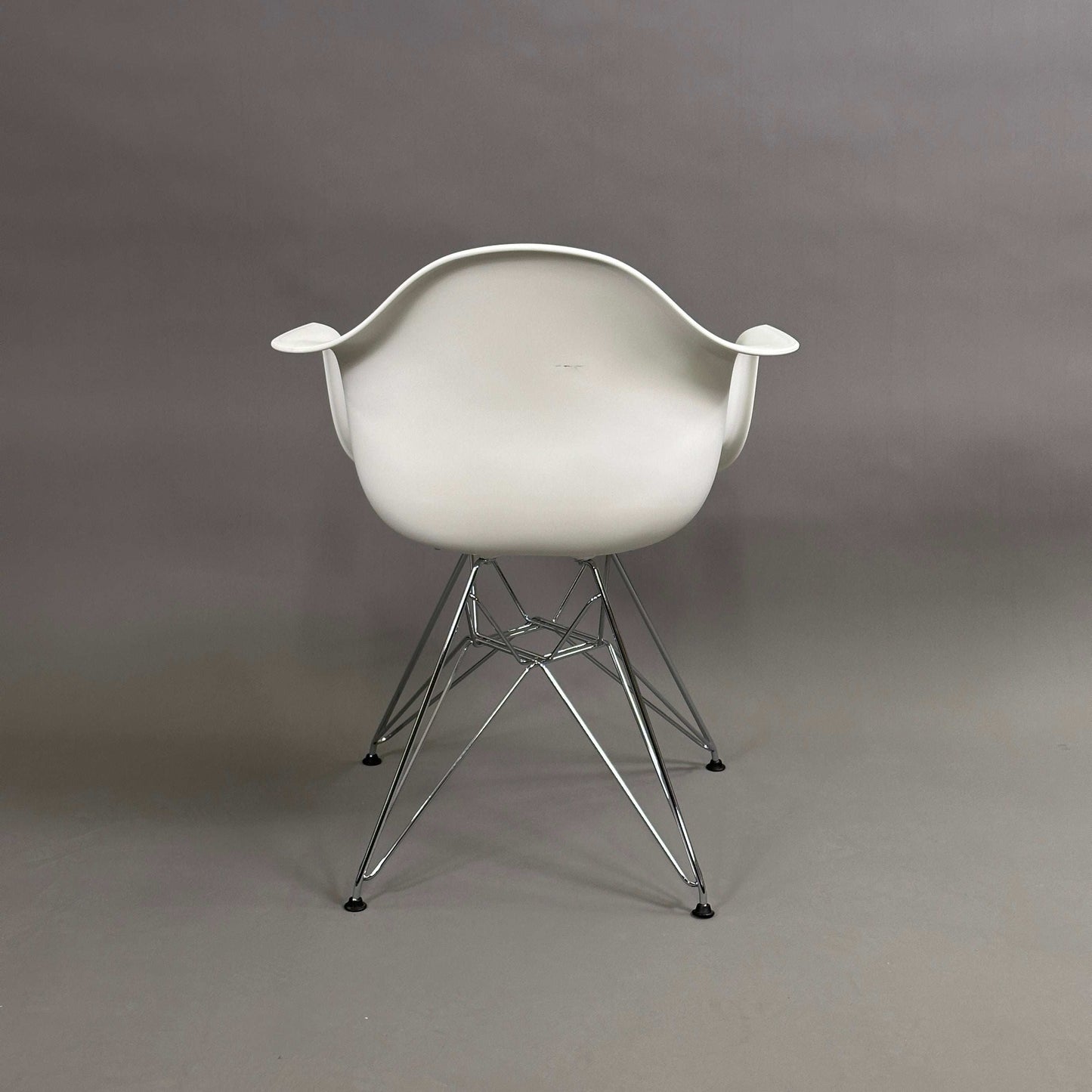 Vitra Eames Plastic Armchair DAR mit weißer Sitzschale und verchromtem Metallgestell ohne Sitzpolster im Studio vor grauem Hintergrund