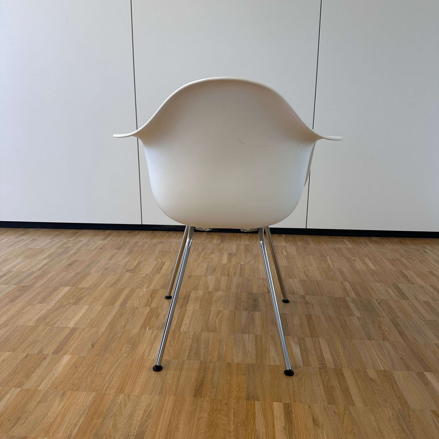 Vitra Eames Plastic Armchair weiß mit verchromtem Metallgestell und ergonomischer Sitzschale aus weißem PE, Rückansicht auf Parkettboden