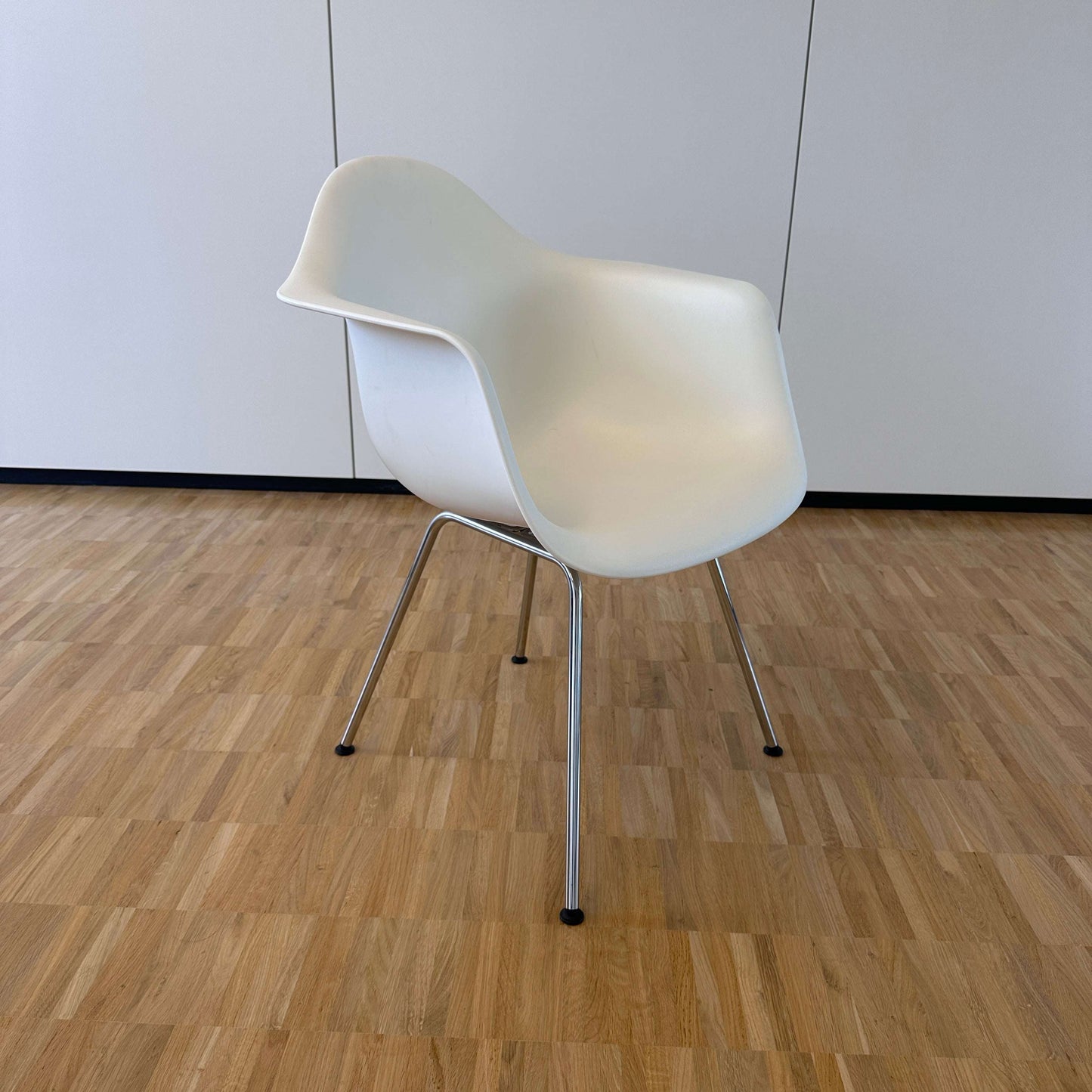 Vitra Eames Plastic Armchair weiß mit weißer PE-Sitzschale und verchromtem Metallgestell auf Holzboden vor weißer Wand