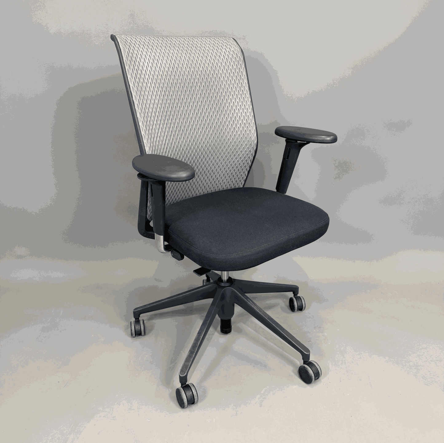 Vitra ID Mesh office chair with black seat, gray mesh backrest, and adjustable 3D armrests on wheels