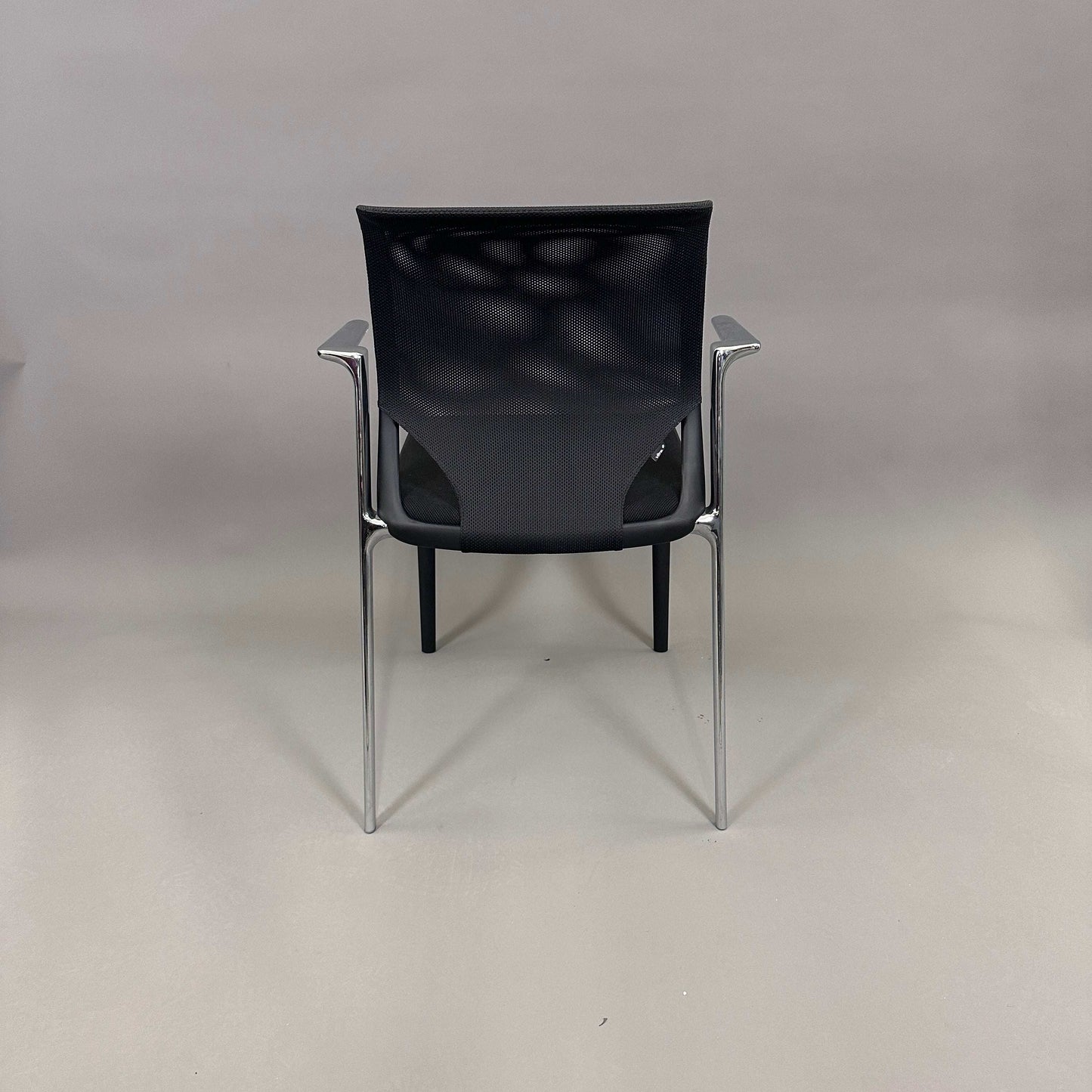 Vitra Medaslim chair with black mesh backrest, padded black seat, and chrome armrests and frame viewed from the back