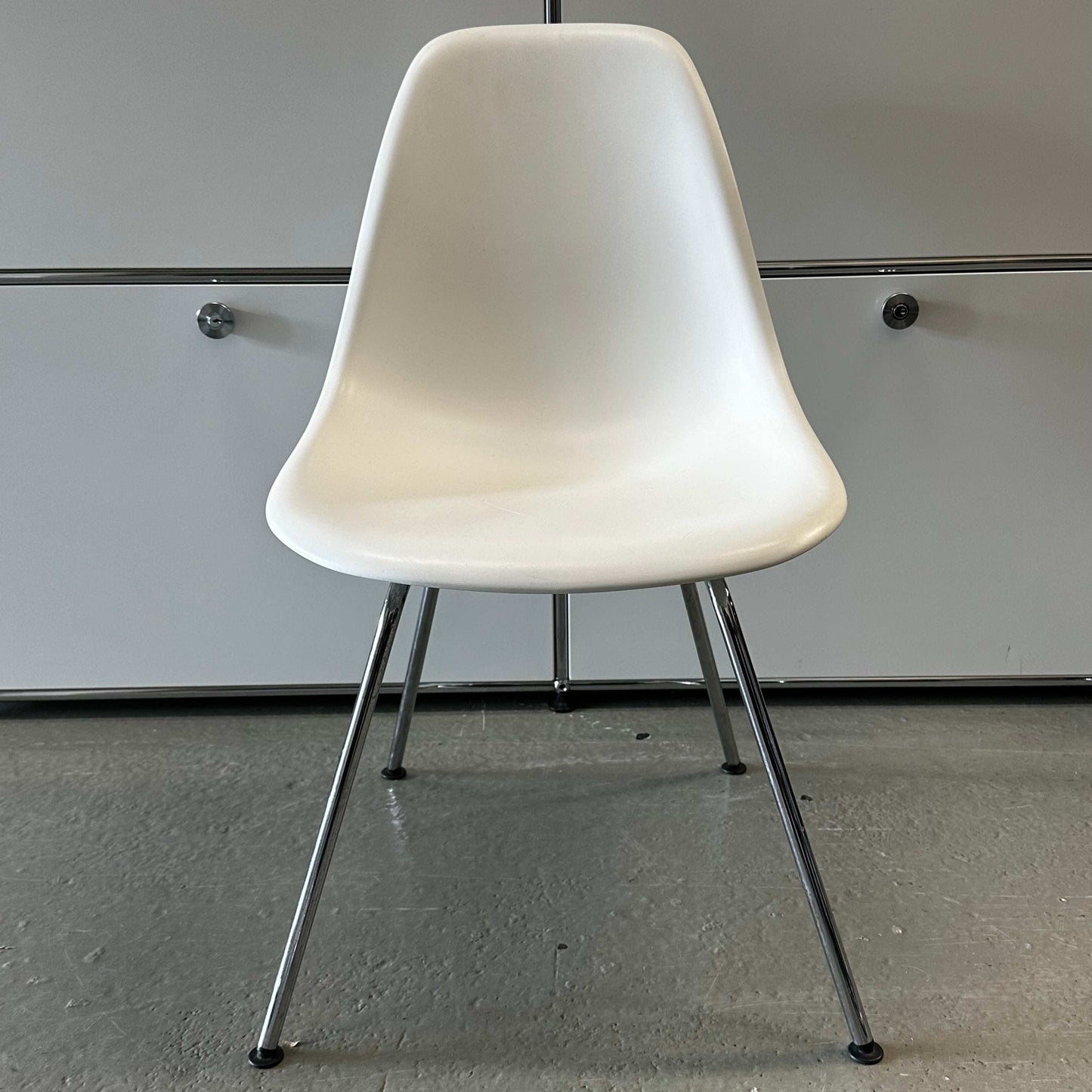 White Vitra Plastic Side Chair with chrome legs and minimalist design against a gray background