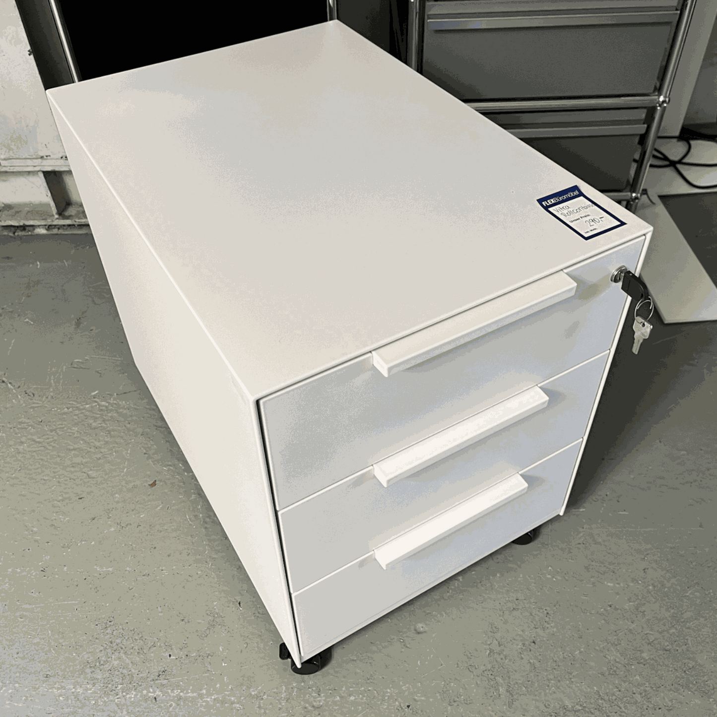 White Vitra Rollcontainer with three drawers, metal body and plastic fronts, dimensions 42x54x61 cm, on casters with key lock.