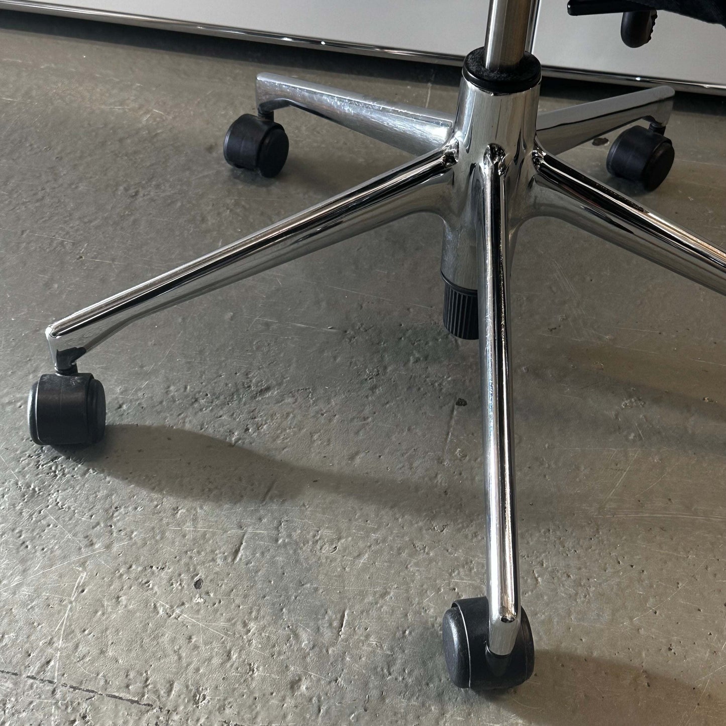 close-up of chrome base and wheels of a Vitra T-Chair Schwarz office chair on textured floor