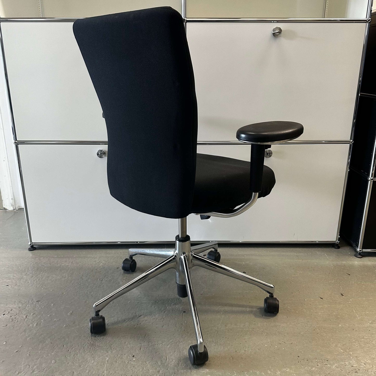 Black Vitra T-Chair with adjustable armrest and chrome base on wheels in modern office setting