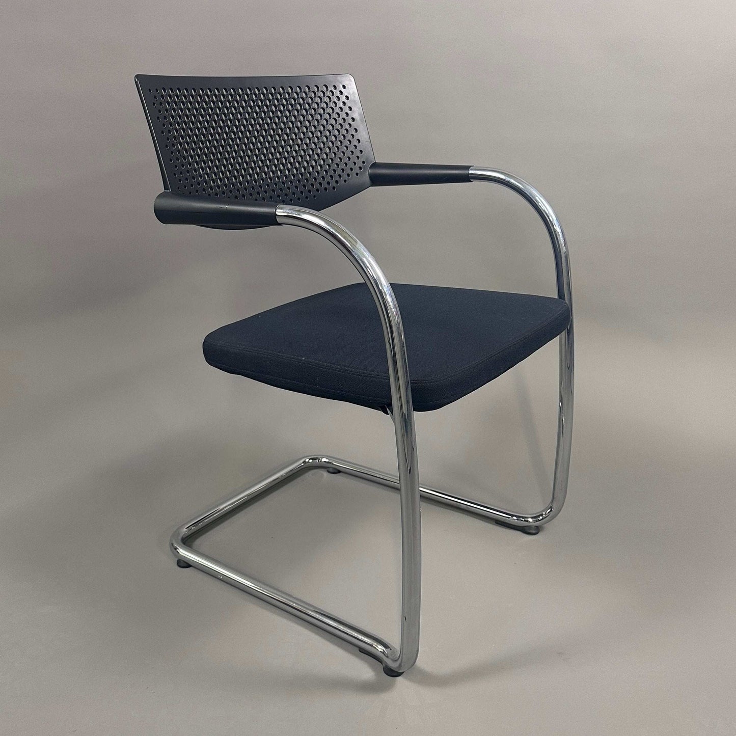 Vitra Visavis 2 black visitor chair with black fabric seat, perforated black plastic backrest, and chrome frame