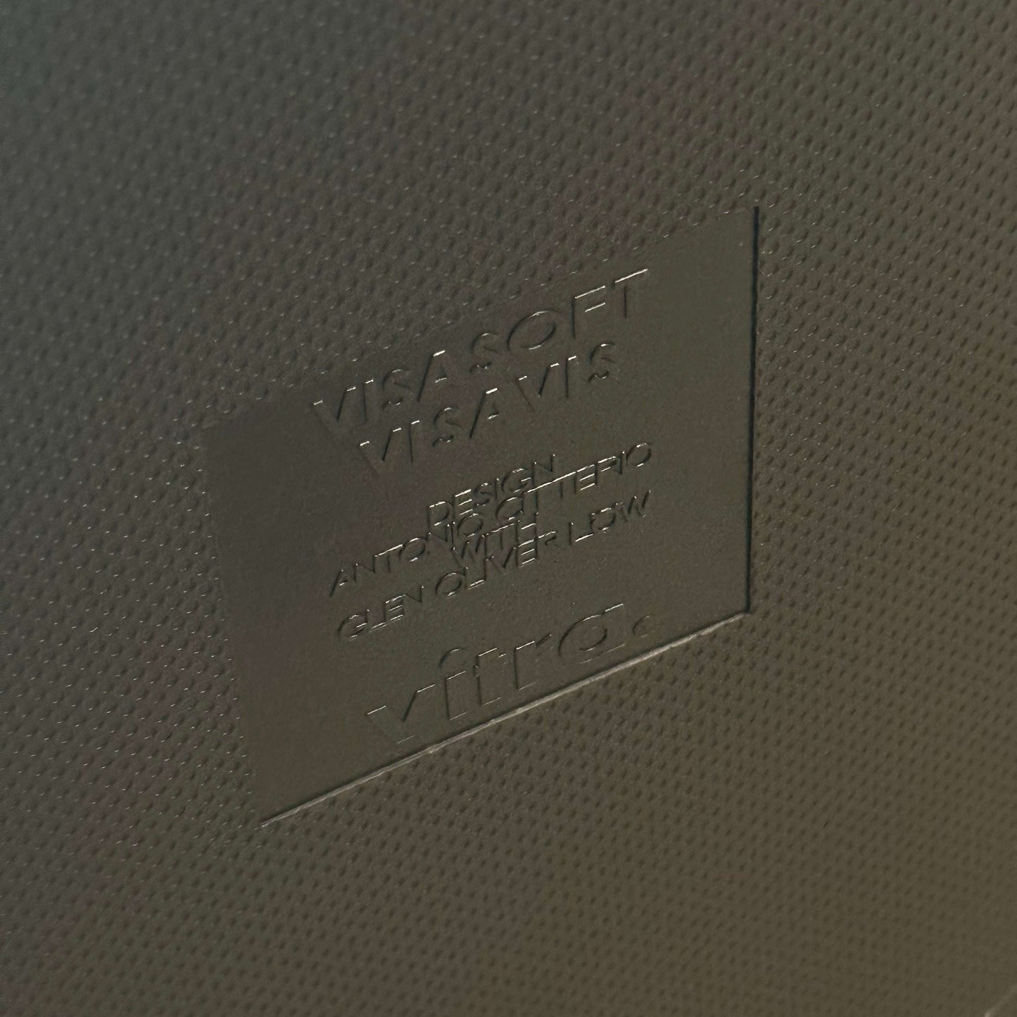 Close-up of embossed Vitra Visavis Softback logo on dark blue textured surface of chair backrest with padded upholstery.