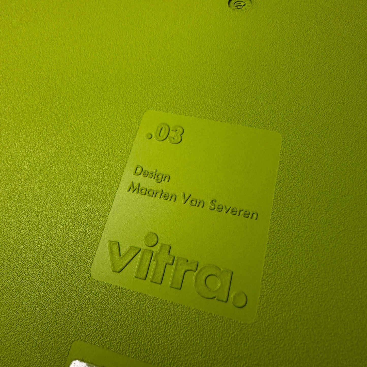 Close-up of Vitra .03 Besucherstuhl avocado chair label with textured plastic surface and embossed designer name Maarten Van Severen.