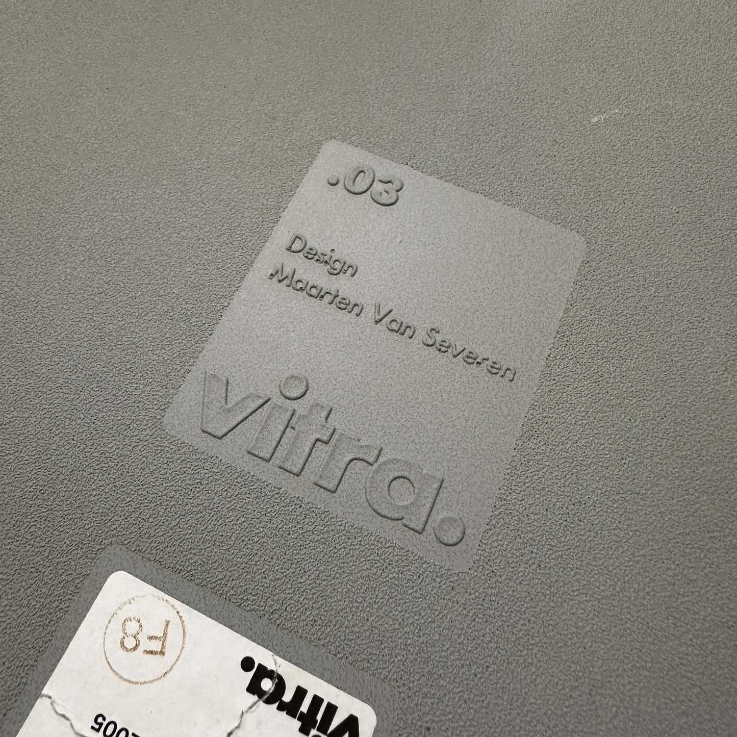 Close-up of the embossed Vitra .03 Besucherstuhl logo on grey plastic chair seat