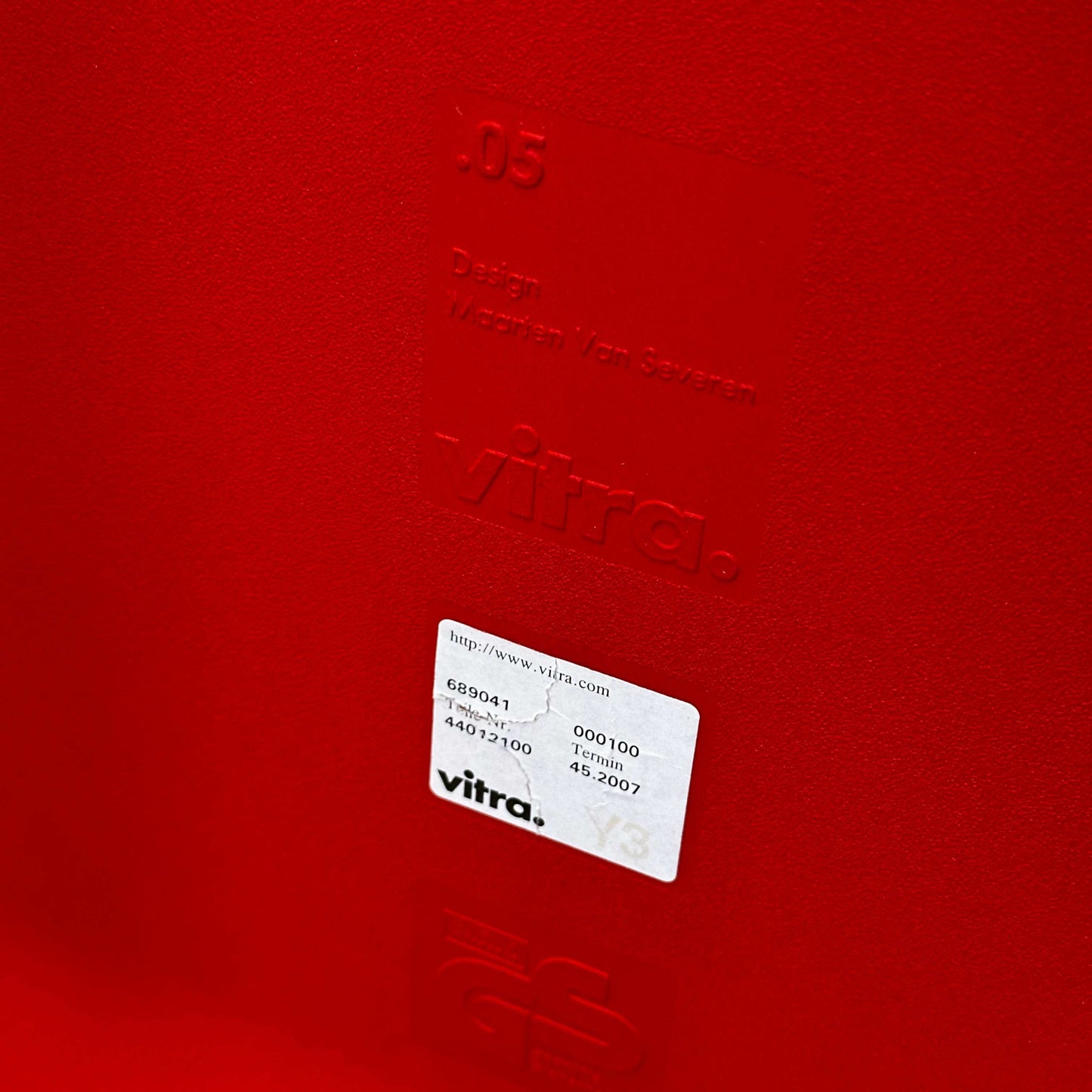 Close-up of the signal red Vitra .05 chair by Maarten van Severen showing embossed branding and label on the polyurethane seat shell.