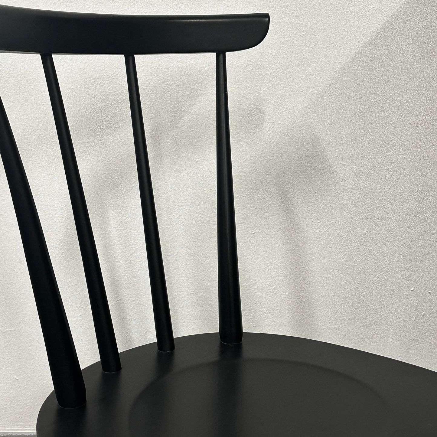 Close-up of the black Wagner W-1960 Chairity with slim vertical backrest slats against a plain wall.