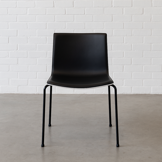 Arper Catifa 46 chair with black leather seat, white shell, and four-leg black frame against white brick wall background