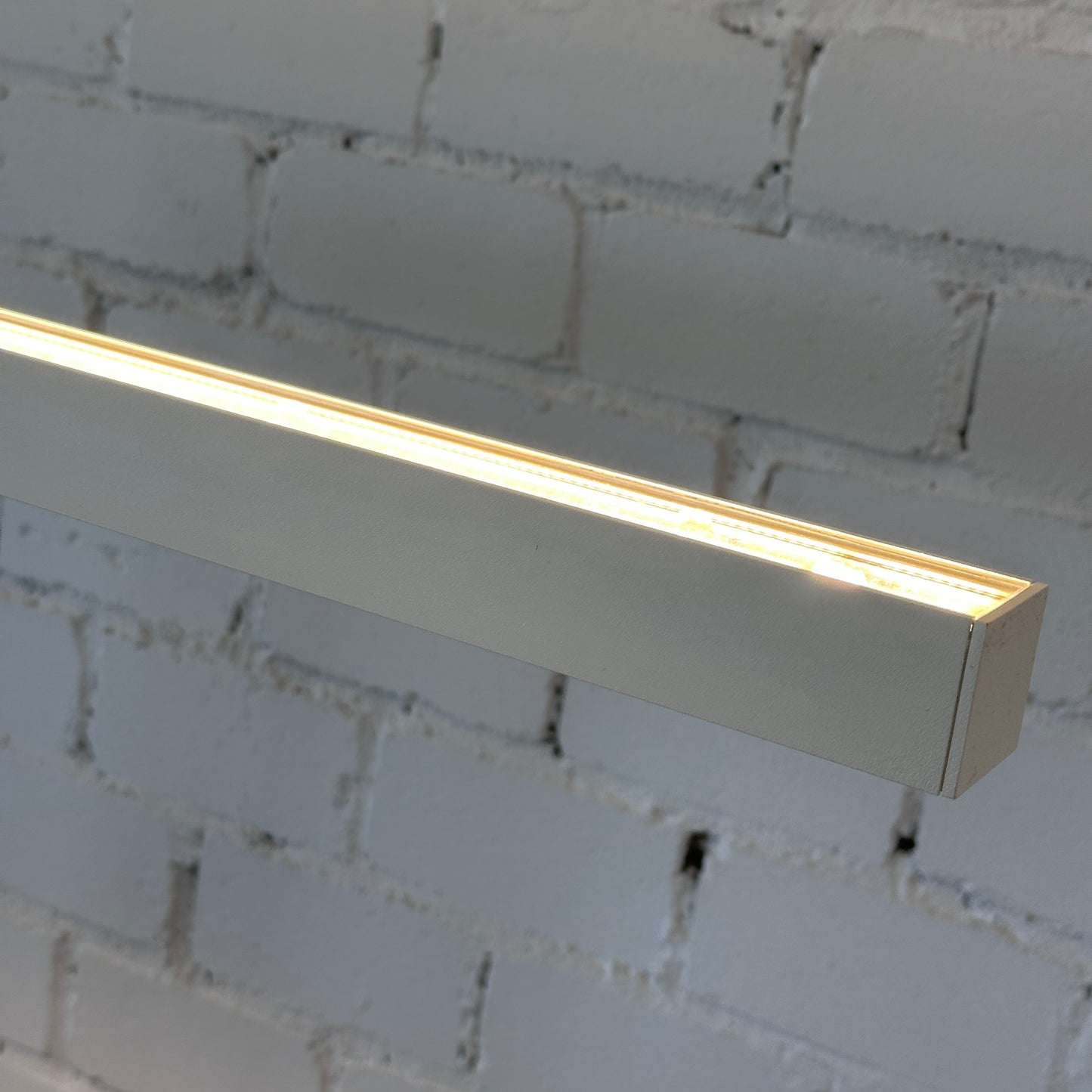 Artemide Econ Office Floor L LED in weißem pulverbeschichtetem Aluminium, leuchtet vor einer weißen Ziegelwand.
