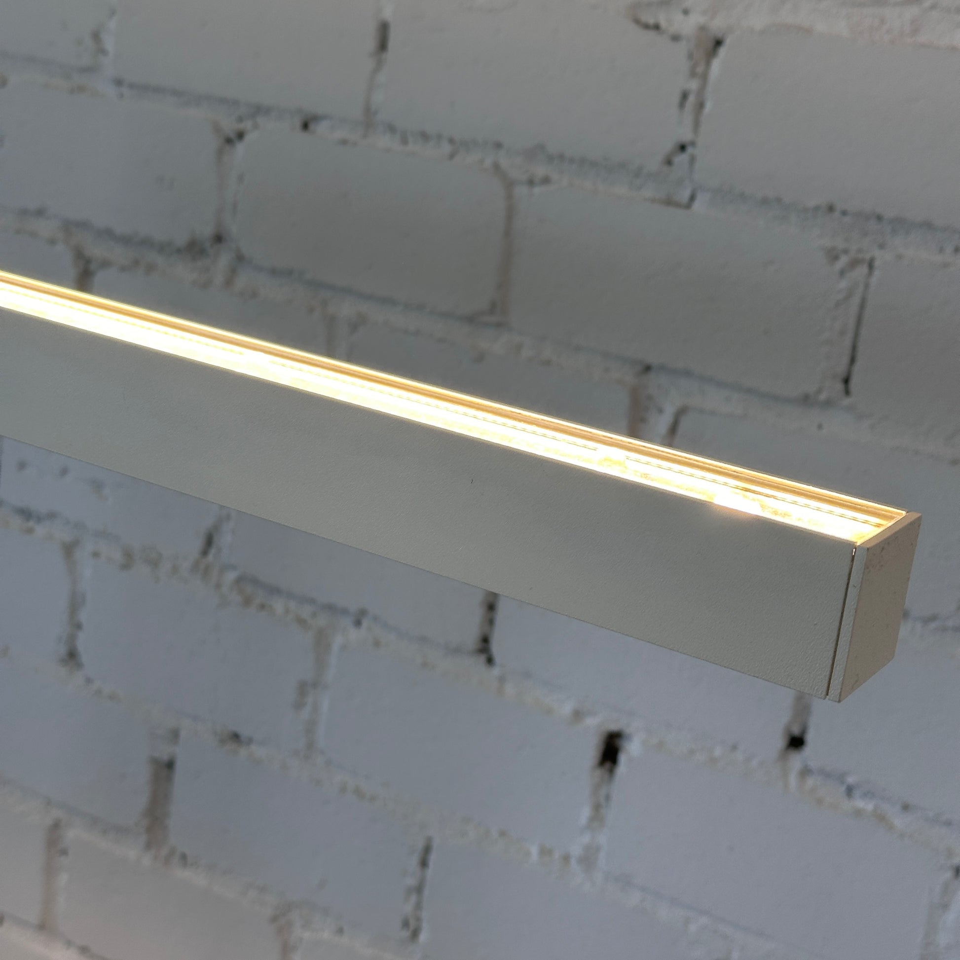 Artemide Econ Office Floor L LED in weißem pulverbeschichtetem Aluminium, leuchtet vor einer weißen Ziegelwand.