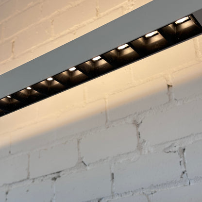 Weiße Artemide Econ Office Floor L LED-Leuchte aus Aluminium mit warmweißem Licht an einer Ziegelwand.
