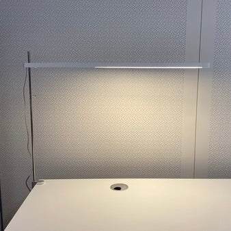 Artemide Talak Tavolo sleek halogen desk lamp with minimalist design on white table against textured wall