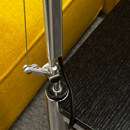 Close-up of silver Artemide Tolomeo Tavolo halogen lamp clamp mounted on black wood table edge near yellow sofa