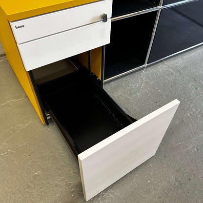 Bene Rollcontainer CT in mustard yellow with white melamine drawers, anthracite fabric seat cushion, three drawers with soft-close and lock, hard caster wheels, and support roller for stability.