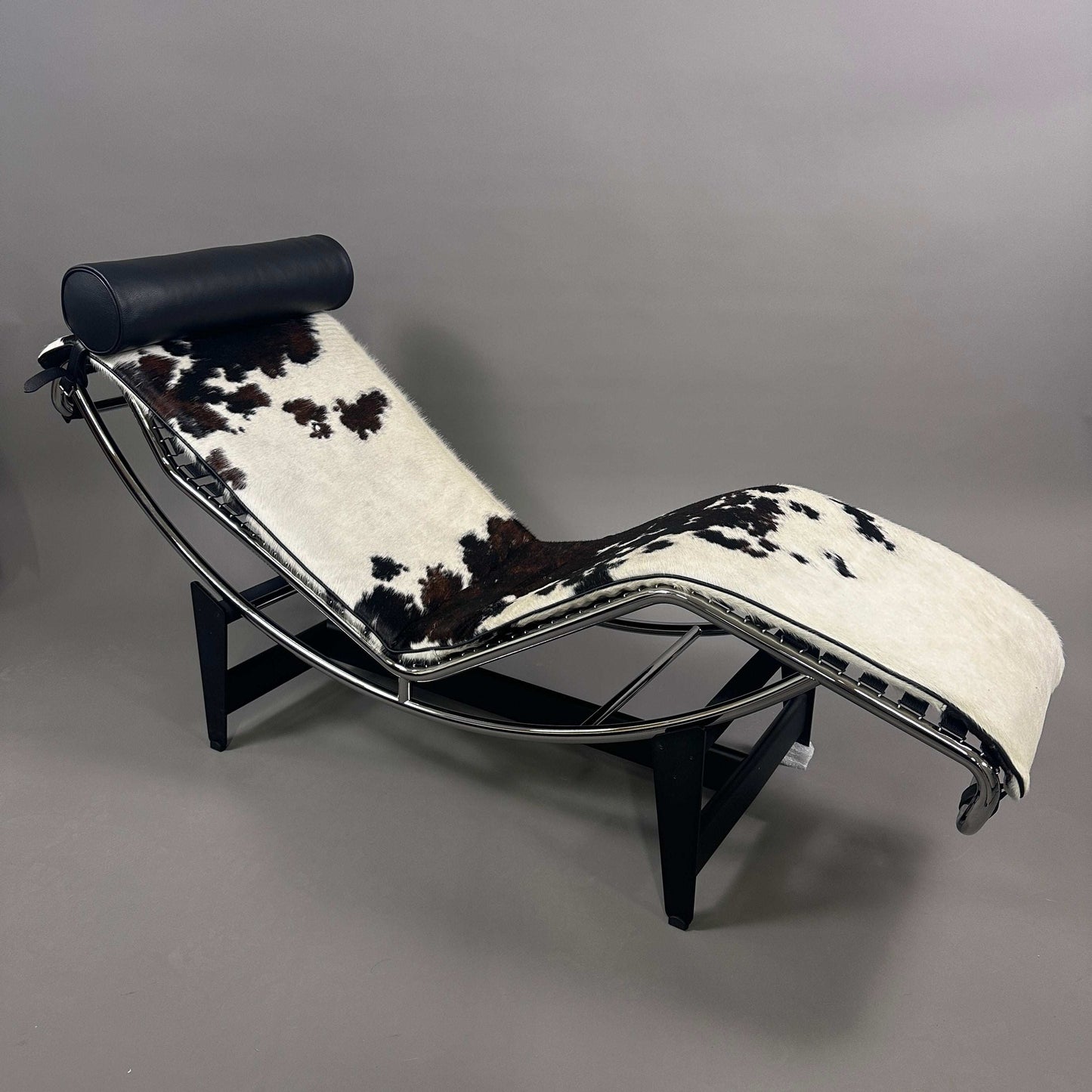 Cassina LC4 Chaiselongue Liege mit schwarz-weiß geflecktem Kuhfell und schwarzer Leder-Nackenrolle, verstellbar, ergonomisches Design, modernes Klassiker-Möbelstück