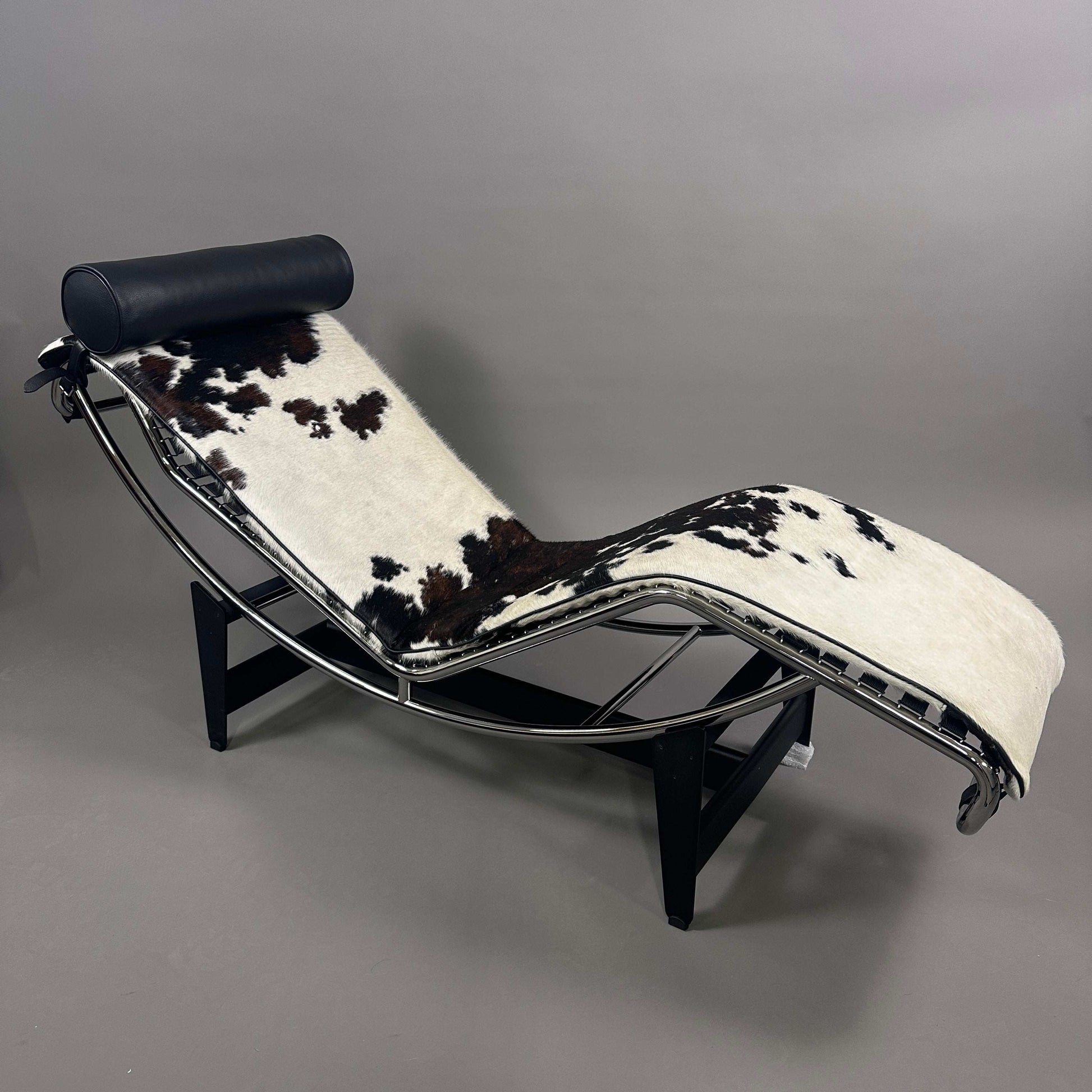 Cassina LC4 Chaiselongue Liege mit schwarz-weiß geflecktem Kuhfell und schwarzer Leder-Nackenrolle, verstellbar, ergonomisches Design, modernes Klassiker-Möbelstück