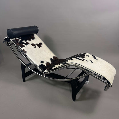 Cassina LC4 Chaiselongue Liege mit schwarz-weiß geflecktem Kuhfell und schwarzer Leder-Nackenrolle, verstellbar, ergonomisches Design, modernes Klassiker-Möbelstück