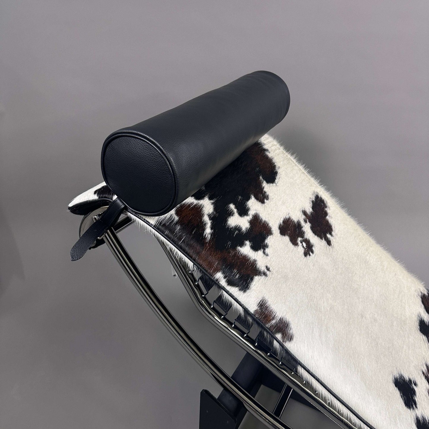 Cassina LC4 Chaiselongue Liege mit schwarz-weiß geflecktem Kuhfellbezug und schwarzer Leder-Nackenrolle auf verstellbarem Chromrahmen
