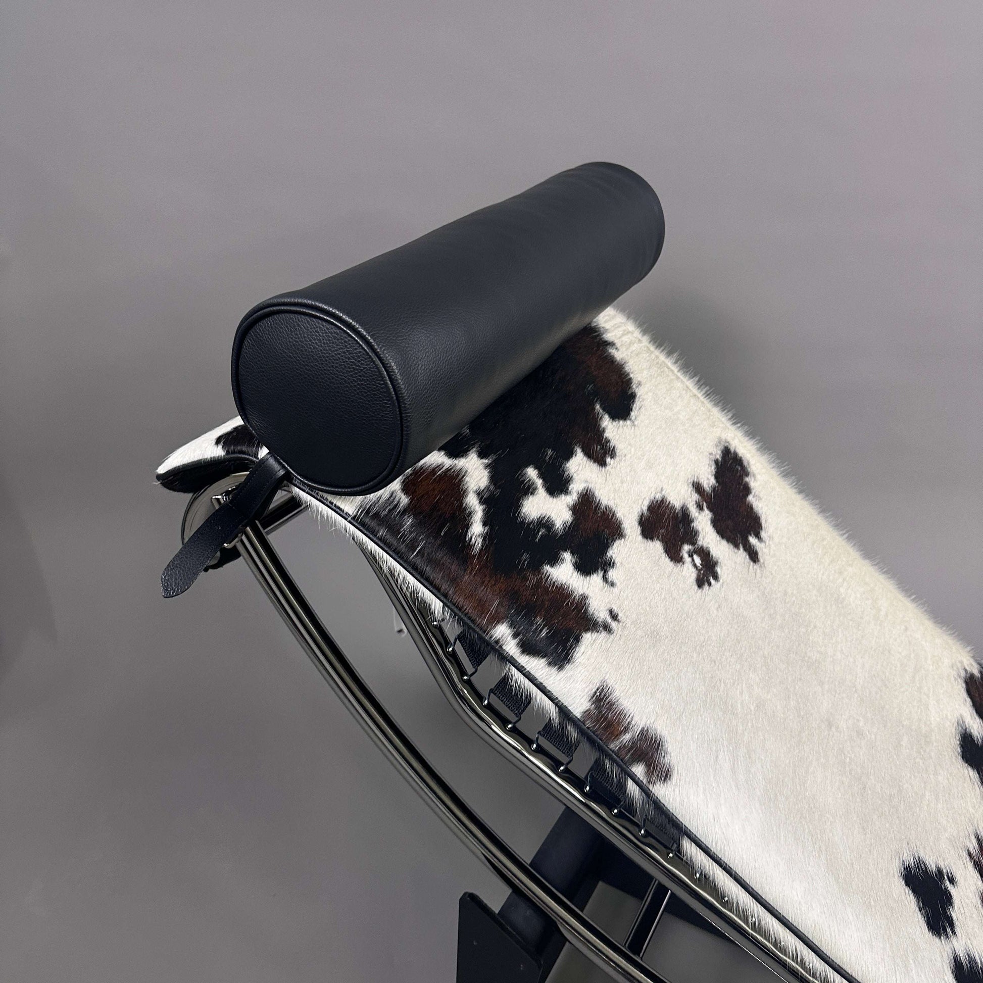 Cassina LC4 Chaiselongue Liege mit schwarz-weiß geflecktem Kuhfellbezug und schwarzer Leder-Nackenrolle auf verstellbarem Chromrahmen