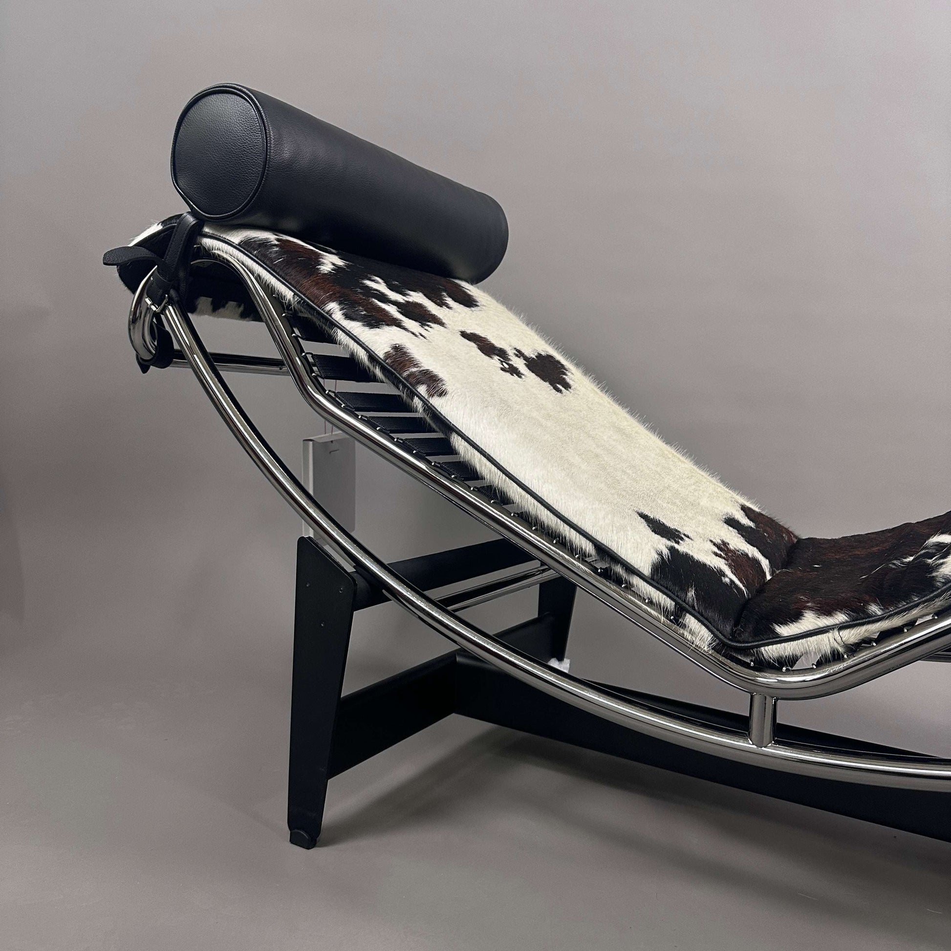 Cassina LC4 Chaiselongue mit ergonomischem Rahmen, Kuhfellbezug schwarz-weiß gefleckt und schwarzer Leder-Nackenrolle