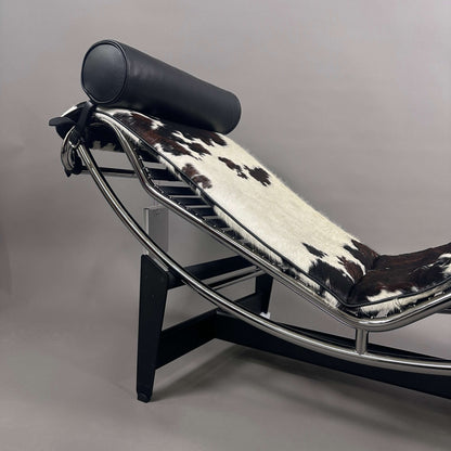 Cassina LC4 Chaiselongue mit ergonomischem Rahmen, Kuhfellbezug schwarz-weiß gefleckt und schwarzer Leder-Nackenrolle