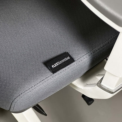 Close-up of ergonomic Bürostuhl seat with grey fabric and white aluminum frame showing FLEXBüromöbel label