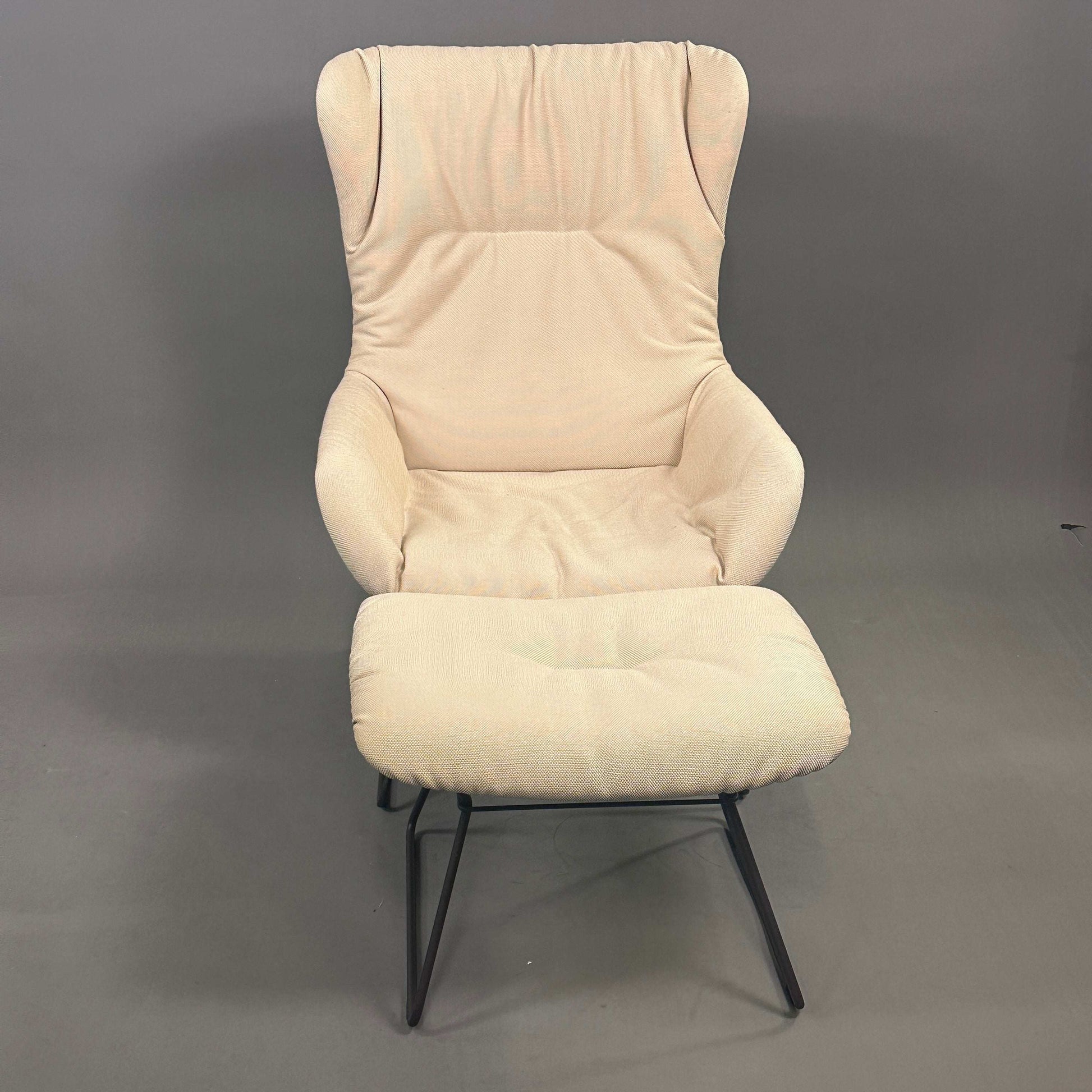 Freifrau Manufaktur Leya Wingback Sessel mit cremefarbenem Stoff und passendem Hocker auf schwarzem Metallgestell