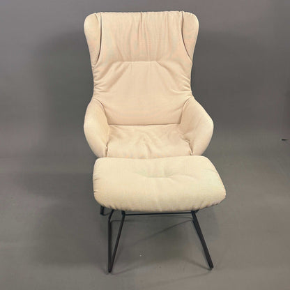 Freifrau Manufaktur Leya Wingback Sessel mit cremefarbenem Stoff und passendem Hocker auf schwarzem Metallgestell