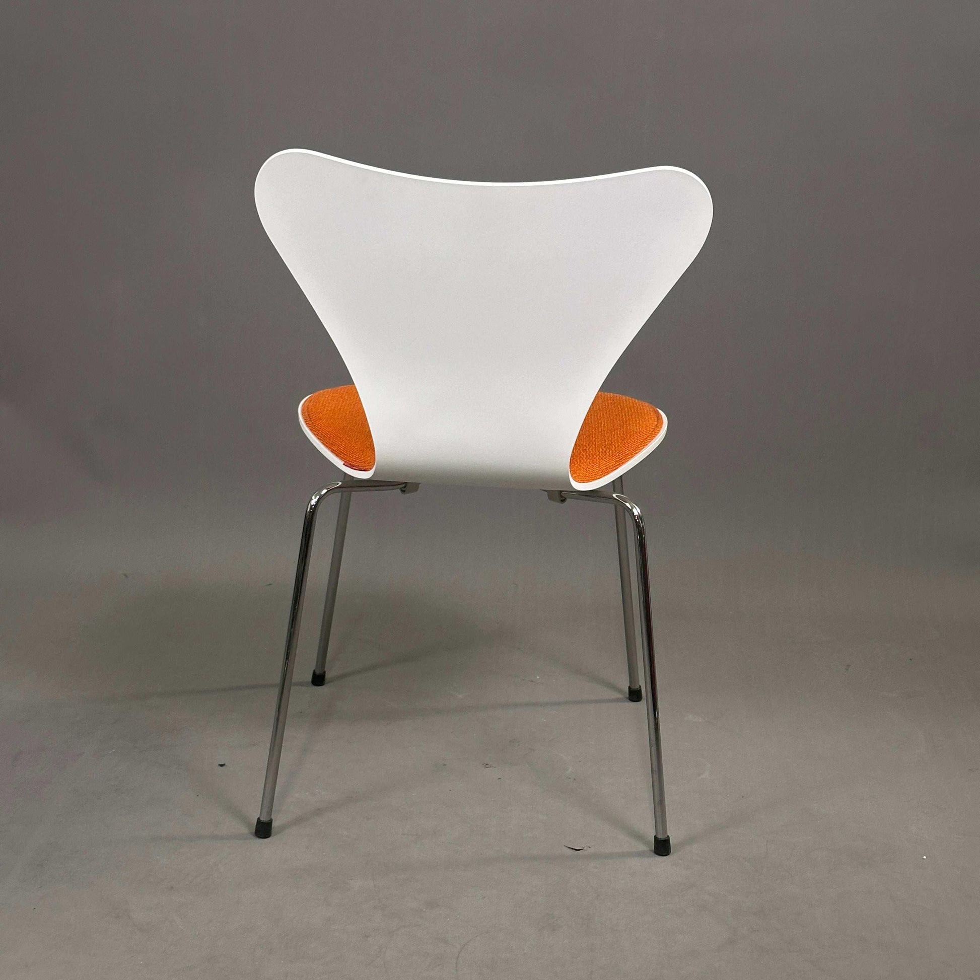 Fritz Hansen Serie 7 Stapelstuhl mit weißer Holzsitzschale, orangefarbener Polsterung und Chromgestell.