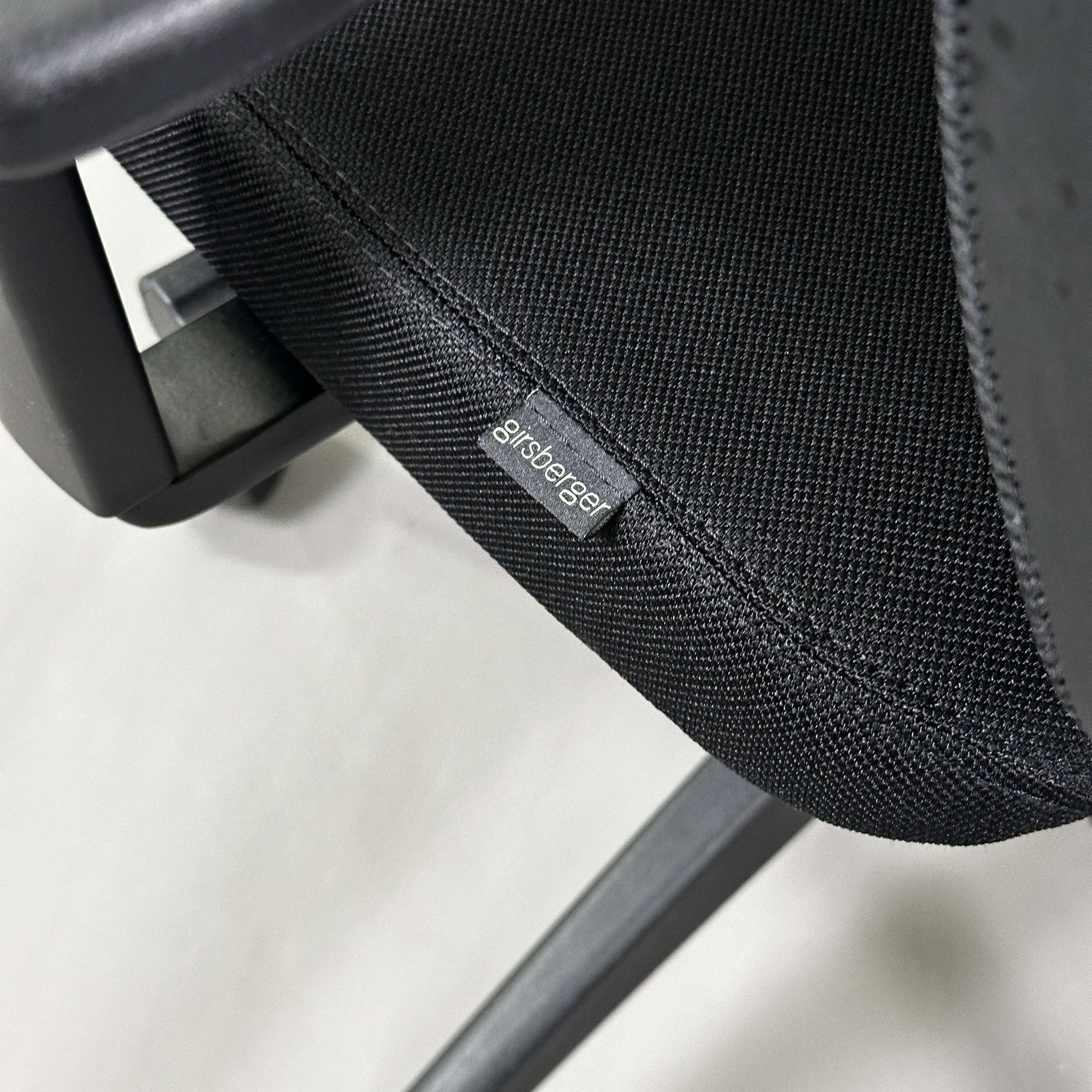 Close-up of black Girsberger Reflex office chair seat with fabric upholstery and mesh backrest showing brand label