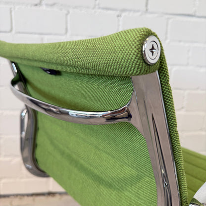 Close-up of Vitra EA 108 Hopsak office chair in green wiesengrün fabric with chrome frame against white brick wall