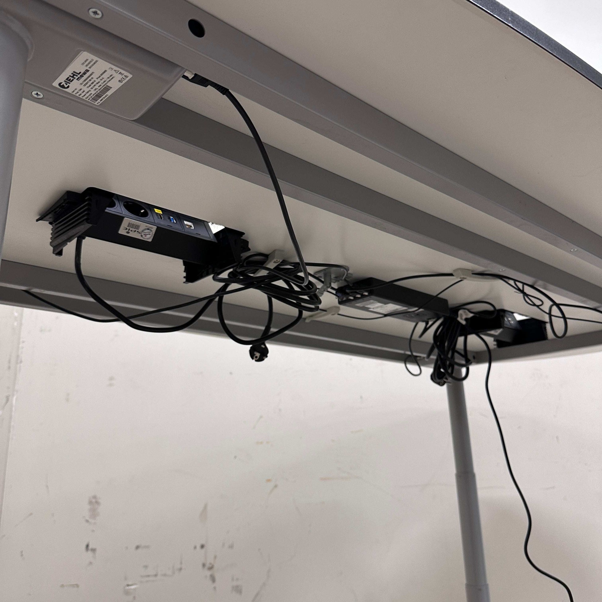 Unterseite eines höhenverstellbaren Konferenztisches 240x120 cm mit Kabelmanagement und Elektrifizierung in Weiß und Silber